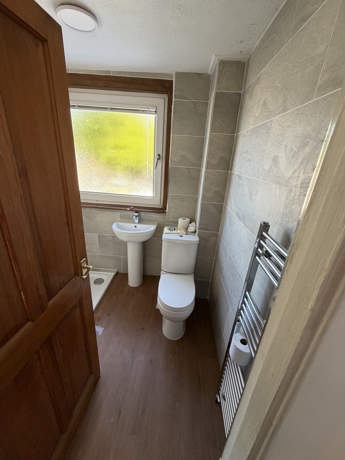 Wider view of the refurbished bathroom with white basin, toilet, grey wall tiles and chrome towel radiator