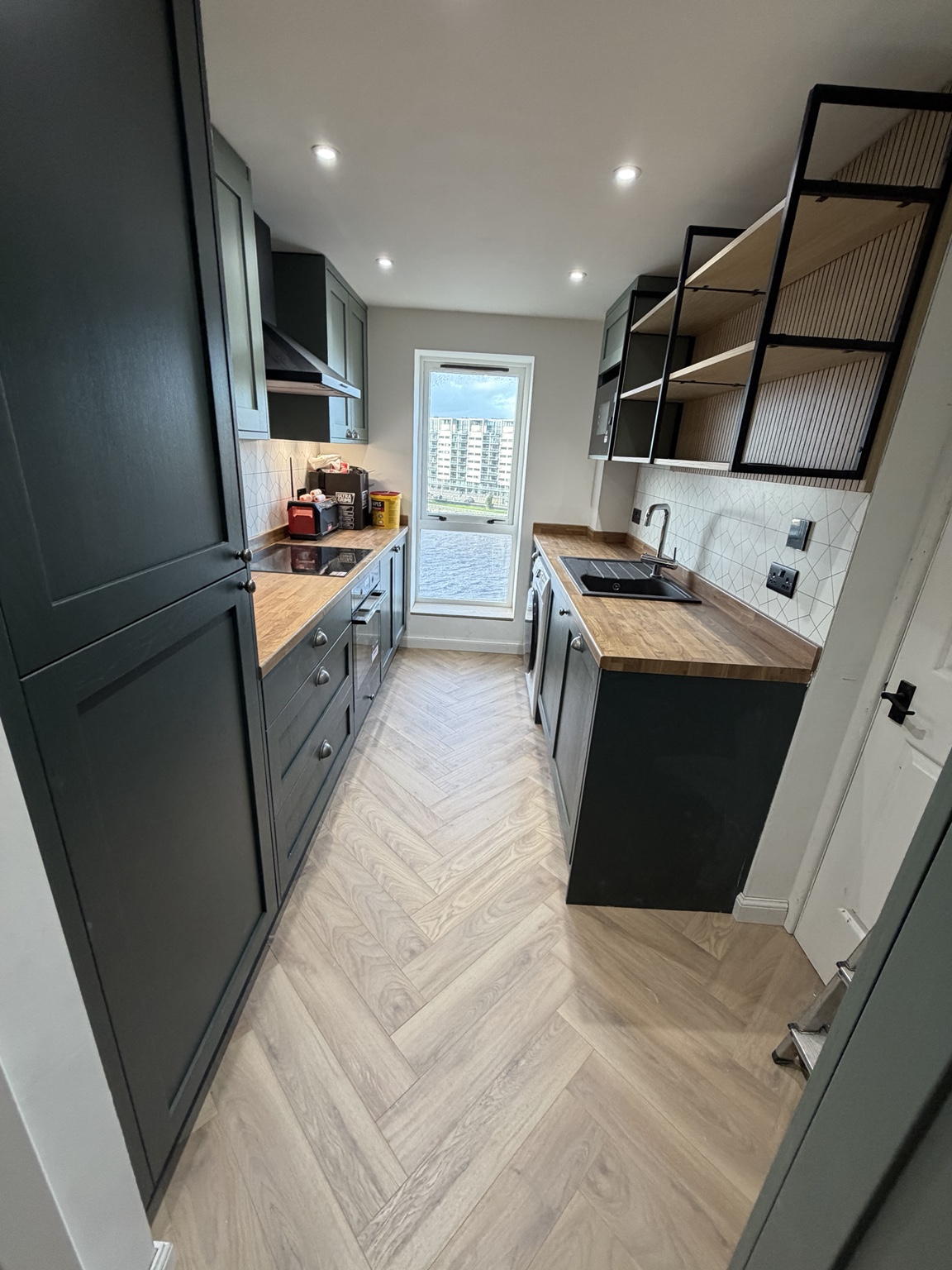 Green shaker kitchen with timber worktops, black fittings and herringbone flooring